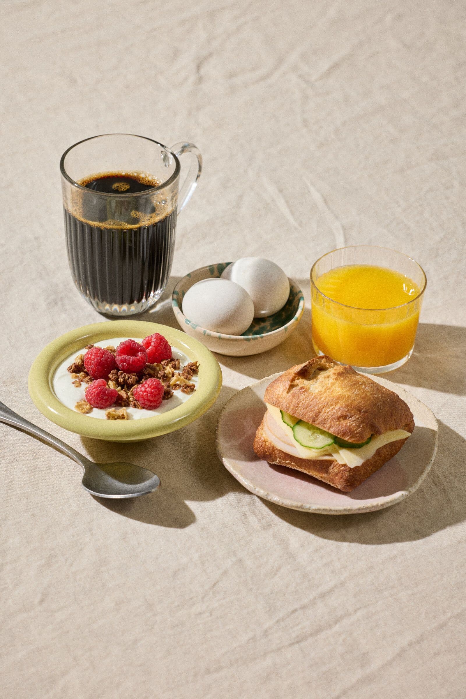 En frukost med kaffe, juice, yoghurt med bär, två ägg och smörgås.