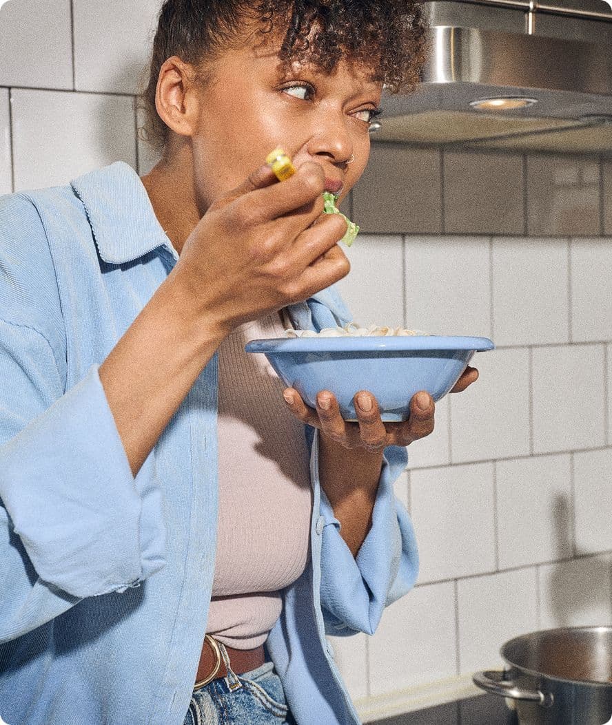 En person äter ur en blå skål med mat i ett kök.